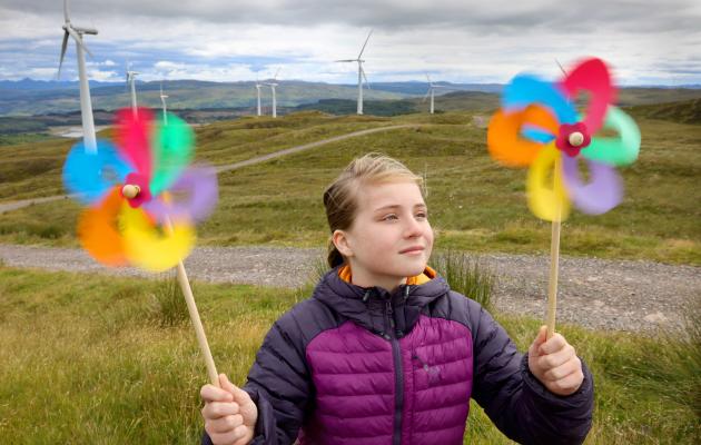 A girl with colourful windmills in front of a windfarm