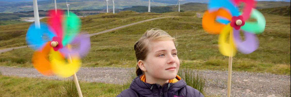A girl with colourful windmills in front of a windfarm